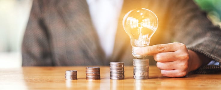 holding glowing lightbulb over coin stack